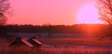 The sun rising over a snowy expanse containing two huts.